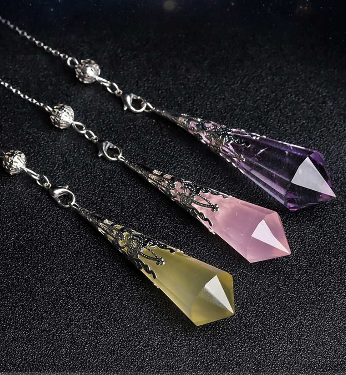 Amethyst, rose quartz and citrine pendulums in an angled tabletop view; one selected option is supplied